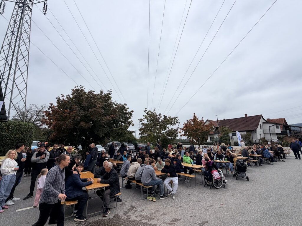 Obiskovalci jubilejnega praznovanja za dolgimi mizami na klubskem dvorišču.